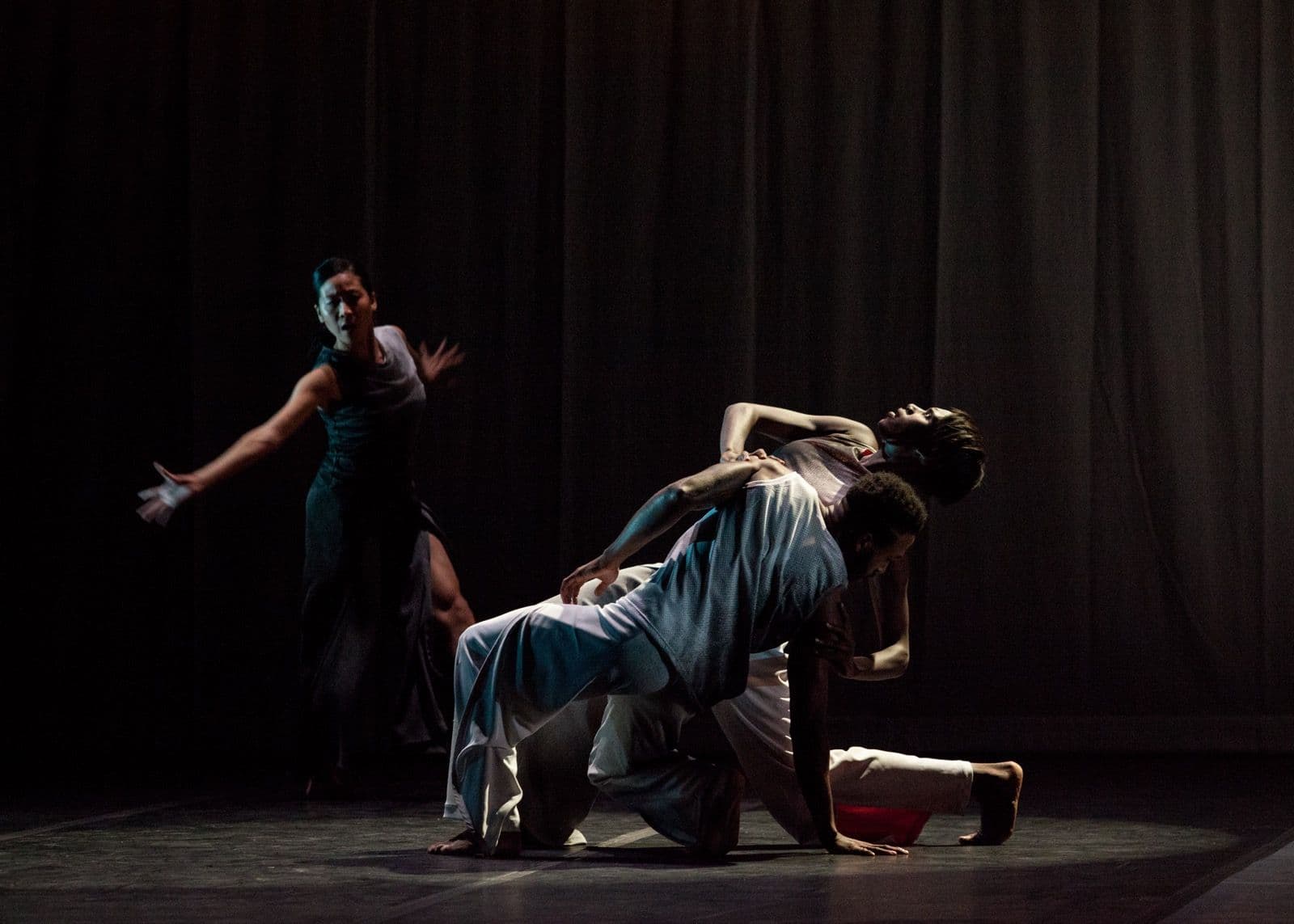 A dancer arches backward supported by another performer while a third dancer reaches out in the background during a stage performance of "Absent Matter."
