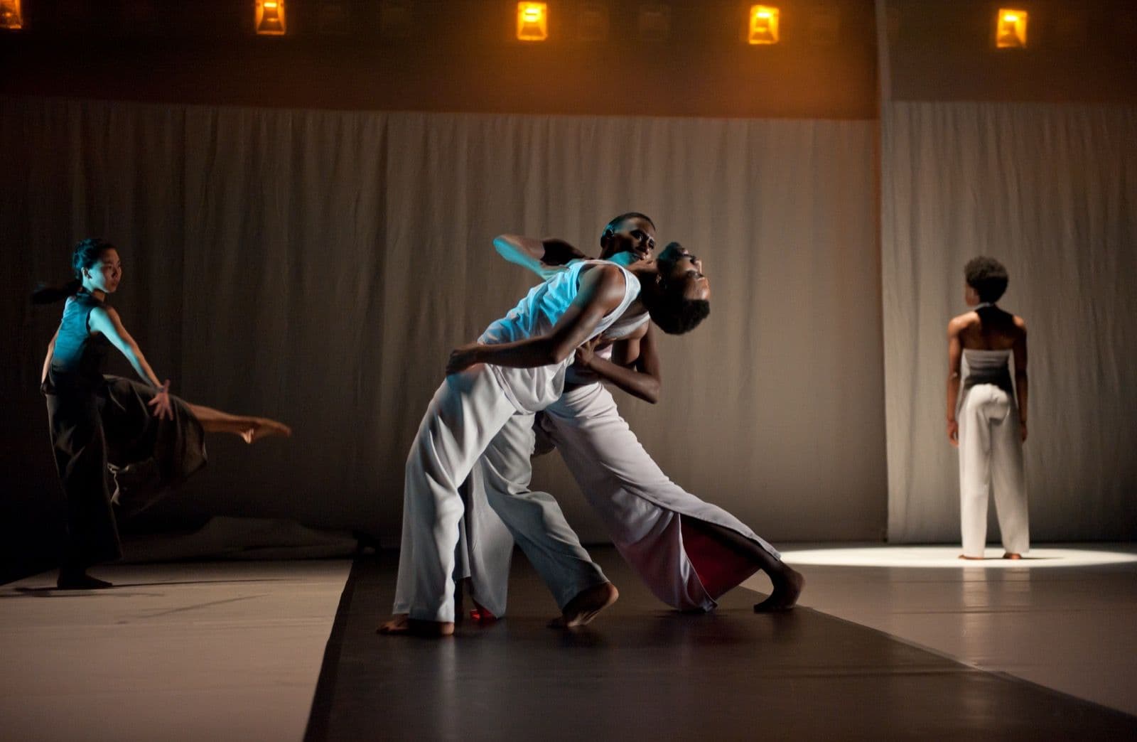 Two main dancers execute an expressive, intertwined duet on stage while ensemble dancers perform in the background.