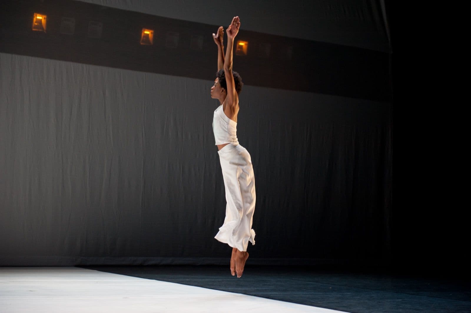 Dancer Tamisha A. Guy leaps straight up into the air with arms extended overhead in a white ensemble performance.