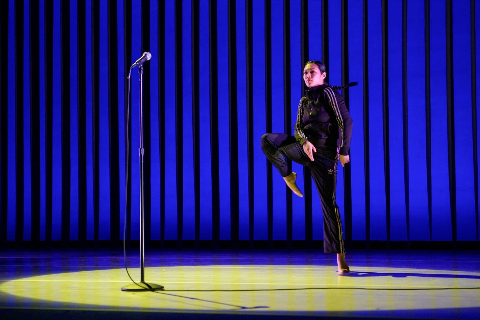 Keerati Jinakunwiphat balances beside a microphone against blue stage lights.