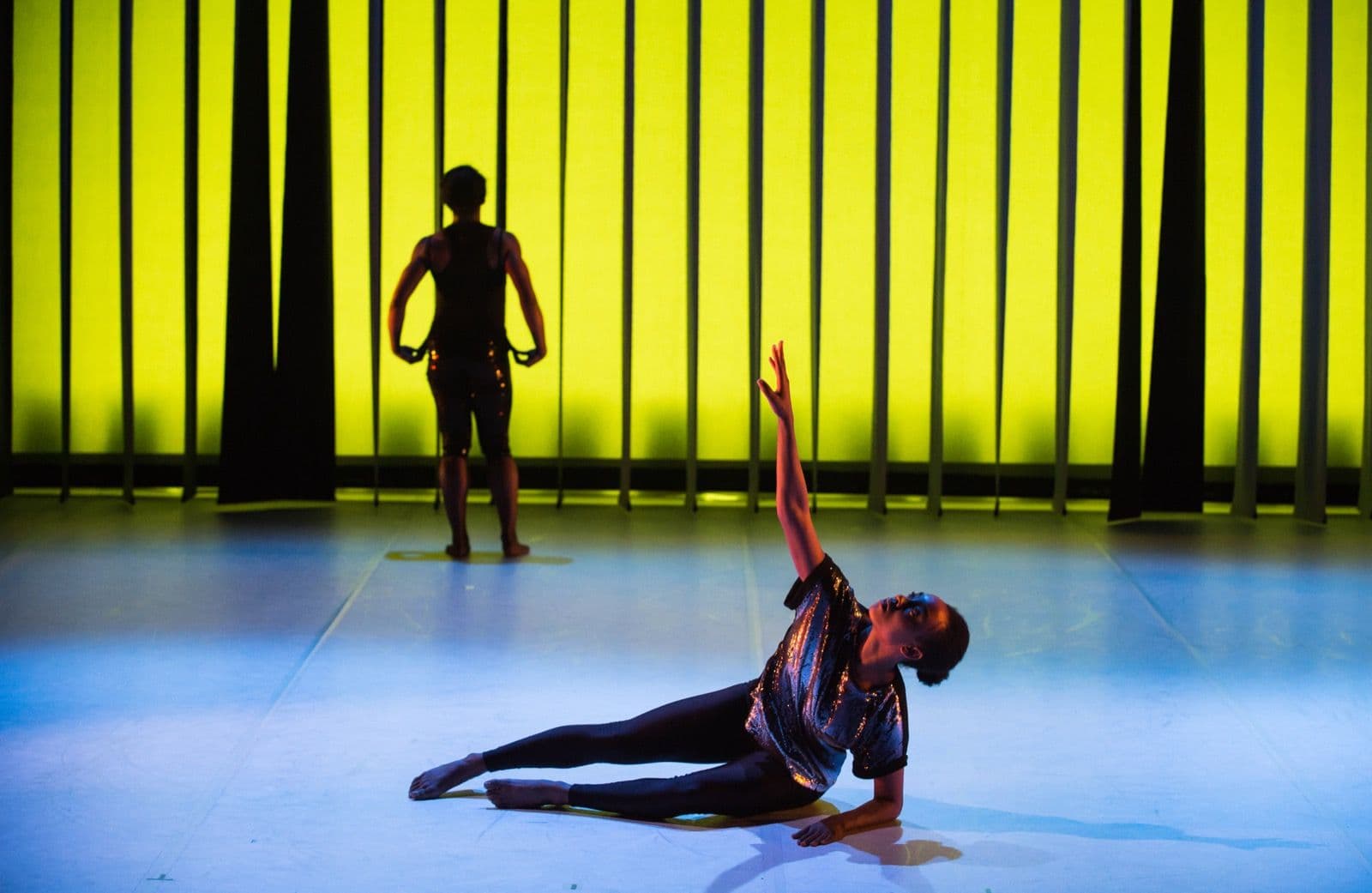 Marcella Lewis performs on the floor as Kayla Farrish stands in silhouette.