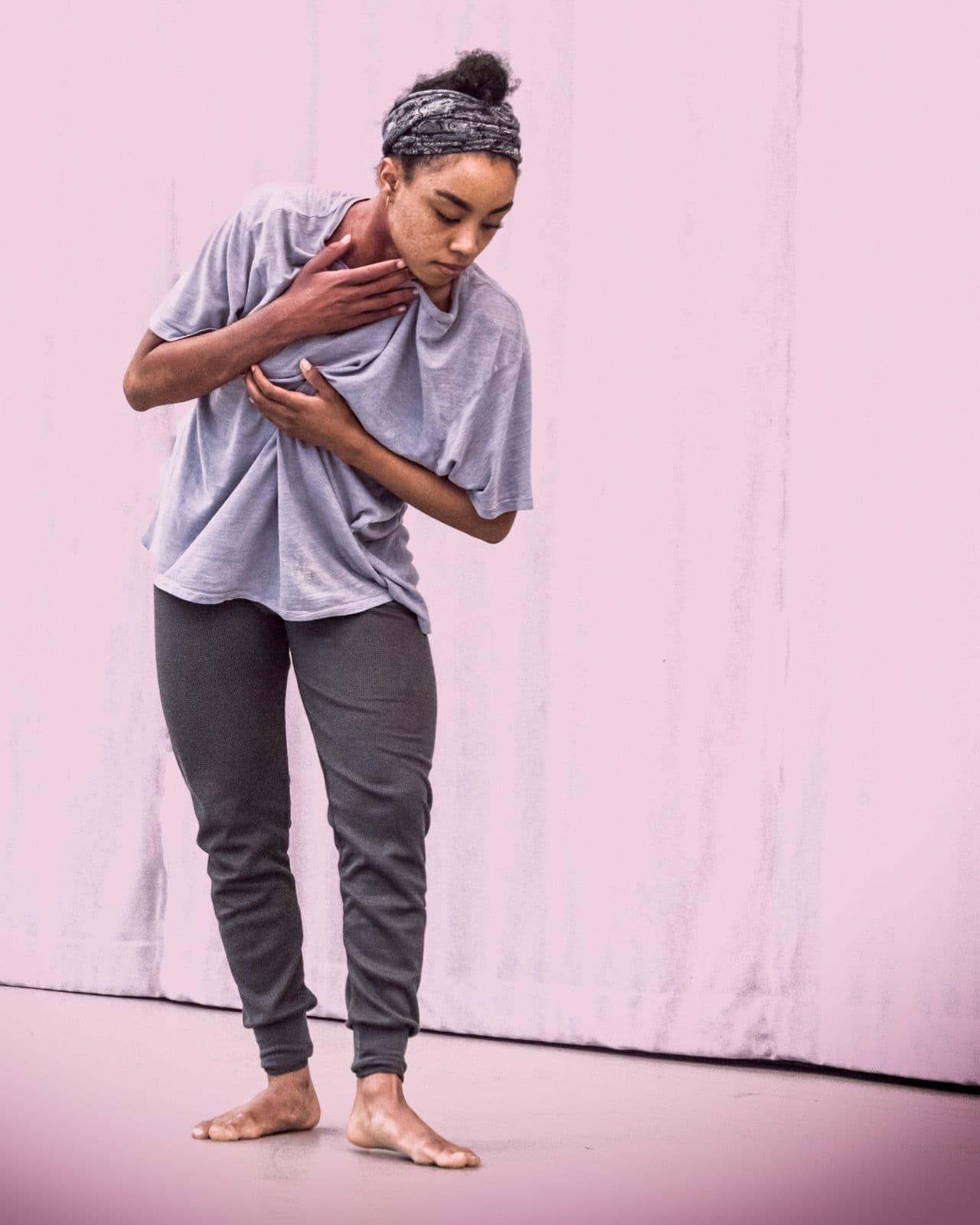 Dancer Marcella Lewis standing in a light purple shirt, holding her chest with eyes looking downward.