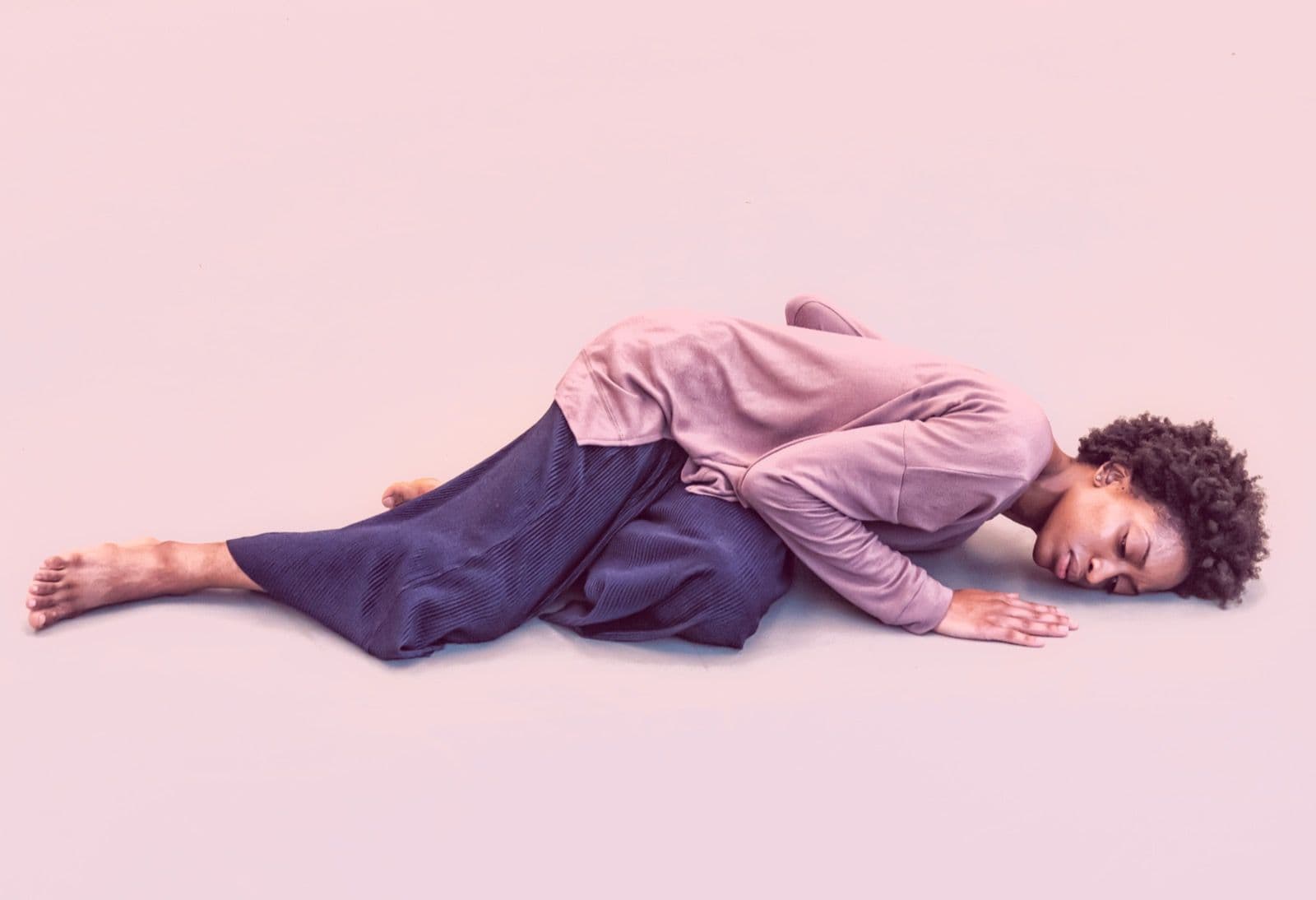 Dancer Tamisha A. Guy lying on her side on the floor with arms tucked in a quiet pose.