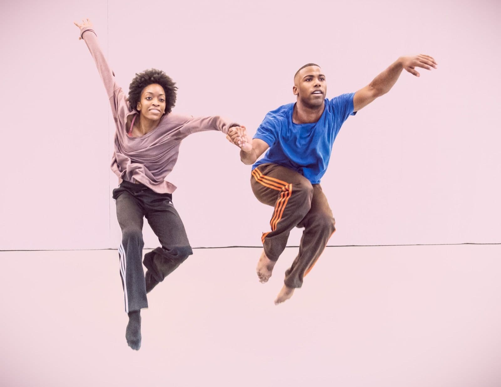 Dancers Tamisha A. Guy and CJ Johnson holding hands mid-air during a dynamic leap.