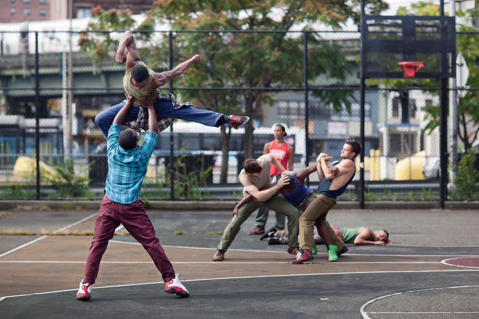 Dancers performing dynamic, physical choreography on an outdoor basketball court.
