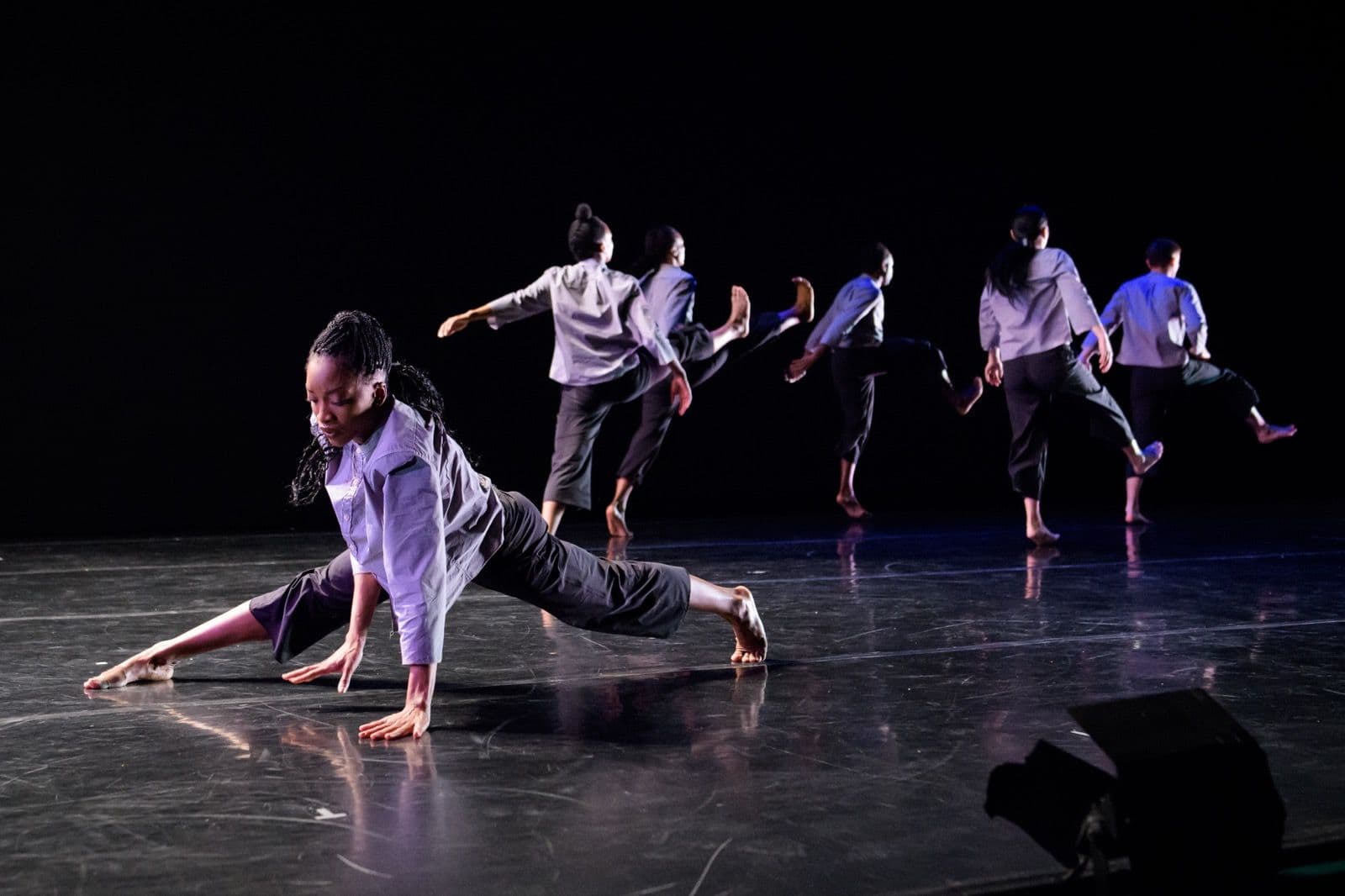 Dancer Tamisha Guy performing a low floor pose in the foreground while ensemble dancers leap and move in the background.