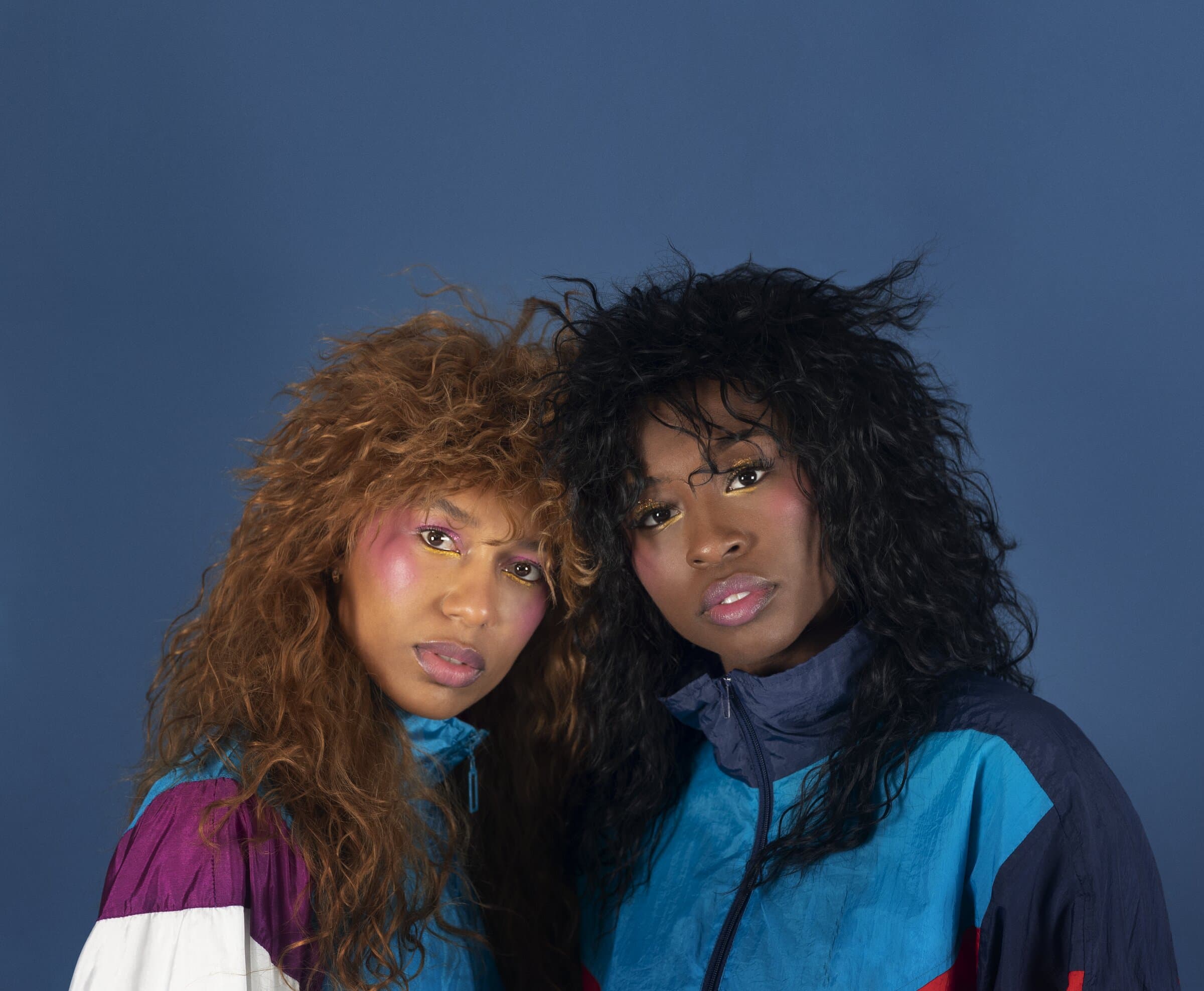 Dancers Catherine Kirk and Faith Joy Mondesire in close-up, wearing colorful retro windbreakers and bold eye makeup, for "Cassette Vol. 1."