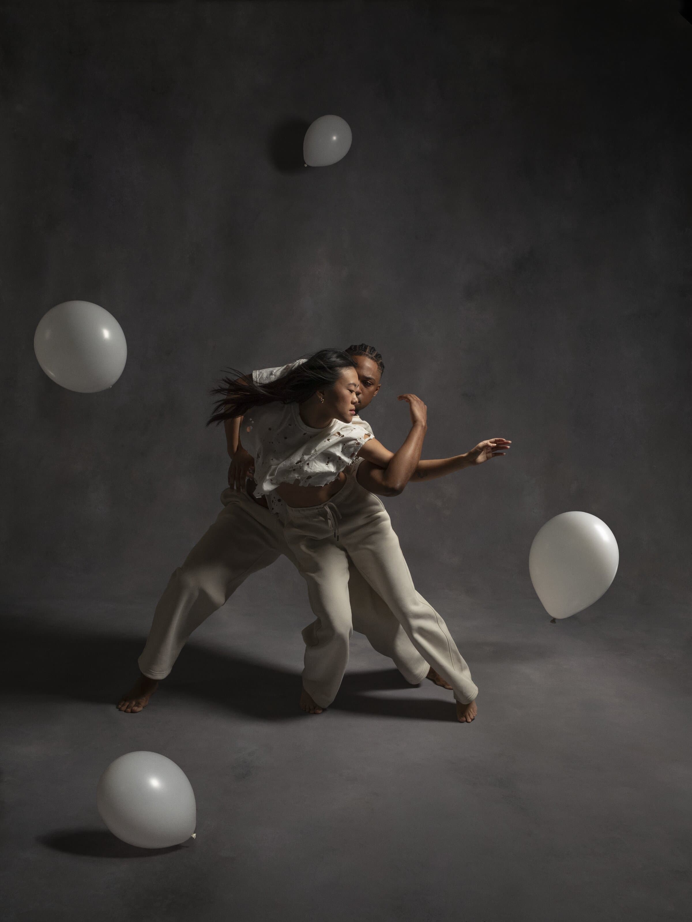 Dancers Destin Morisset and Olivia Wang dancing together in distressed white clothing amid floating white balloons in "White Space."