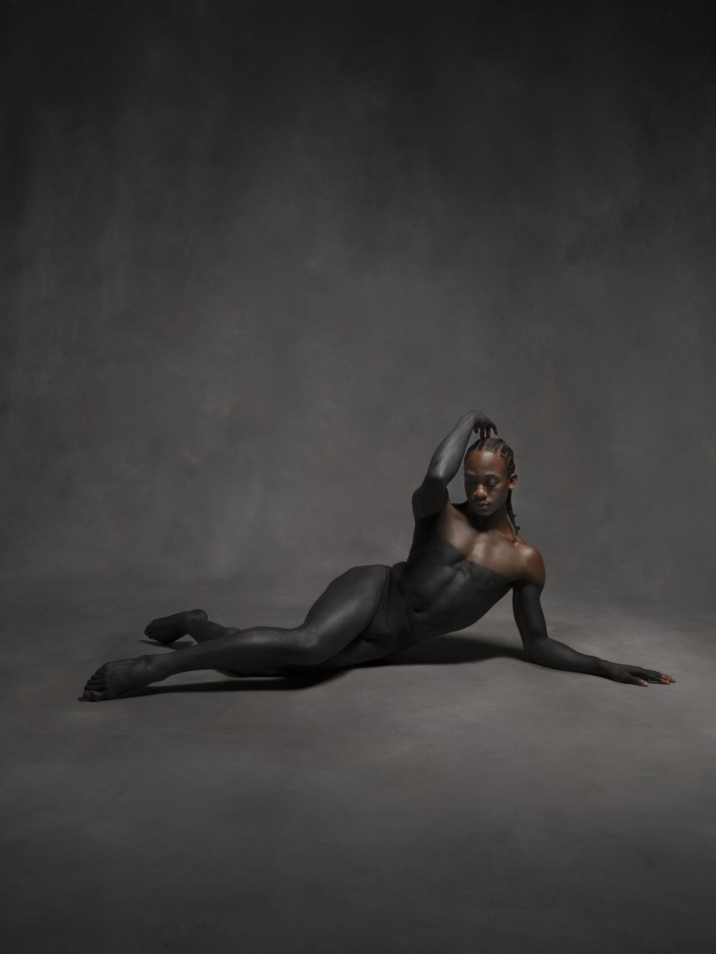 Dancer Mykiah Goree reclining on the floor, one arm raised behind his head, in dramatic low-key lighting.