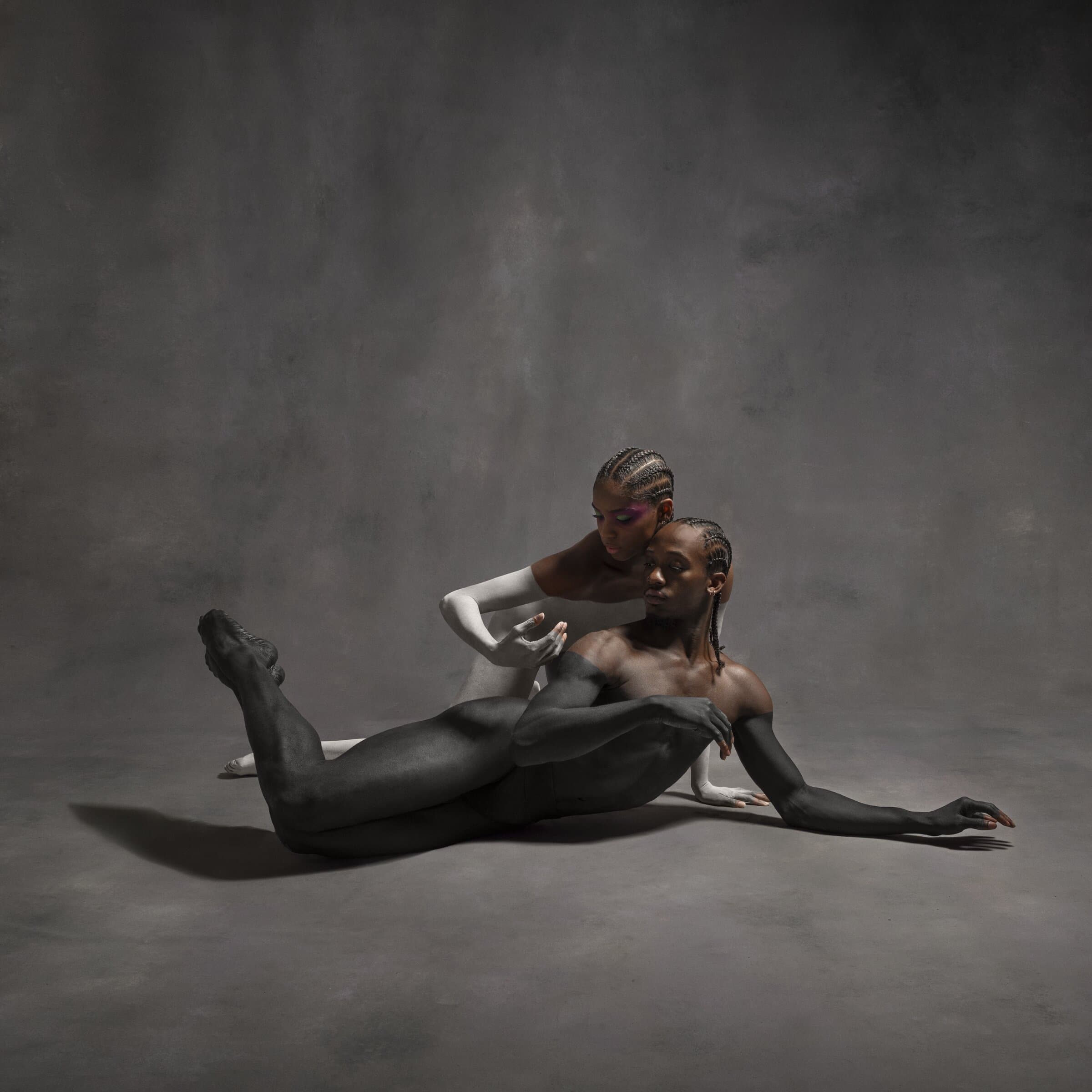 Dancers Mykiah Goree and Niya Smith entwined on the floor in "White Space," moody studio lighting.